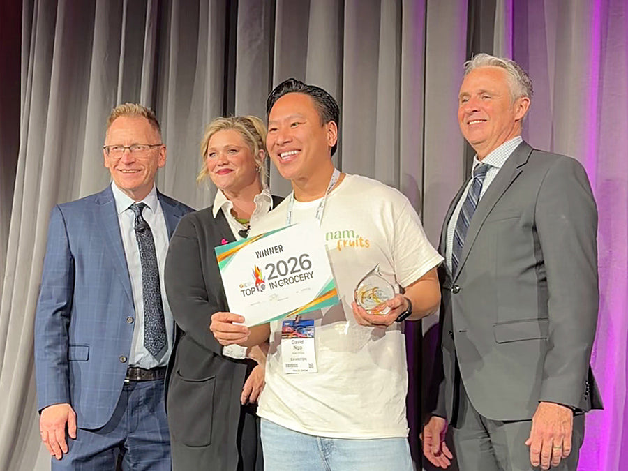 David Ngo on stage at Grocery Innovations Canada 2026 holding the Top 10 in Grocery winner sign, with the award presenters