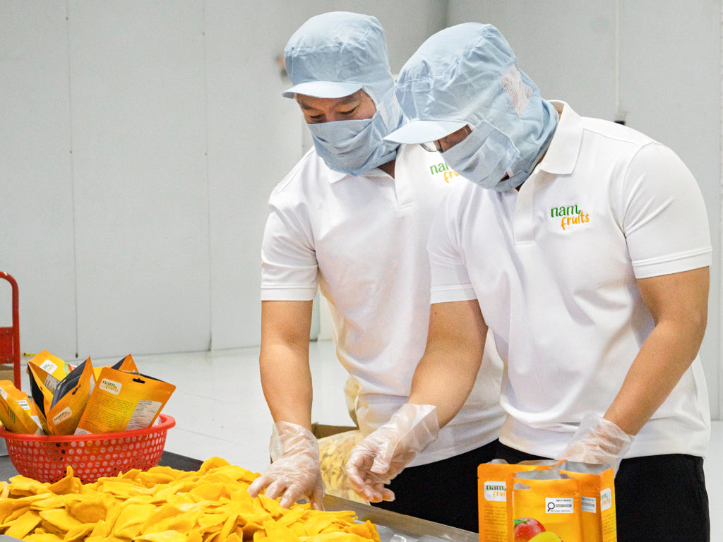 Workers in hairnets and masks packing dried mango pouches at the factory in Vietnam